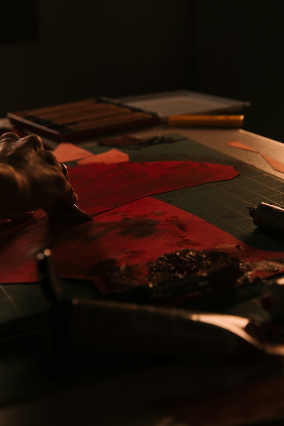 A hand applies leather finish to a piece of red leather.