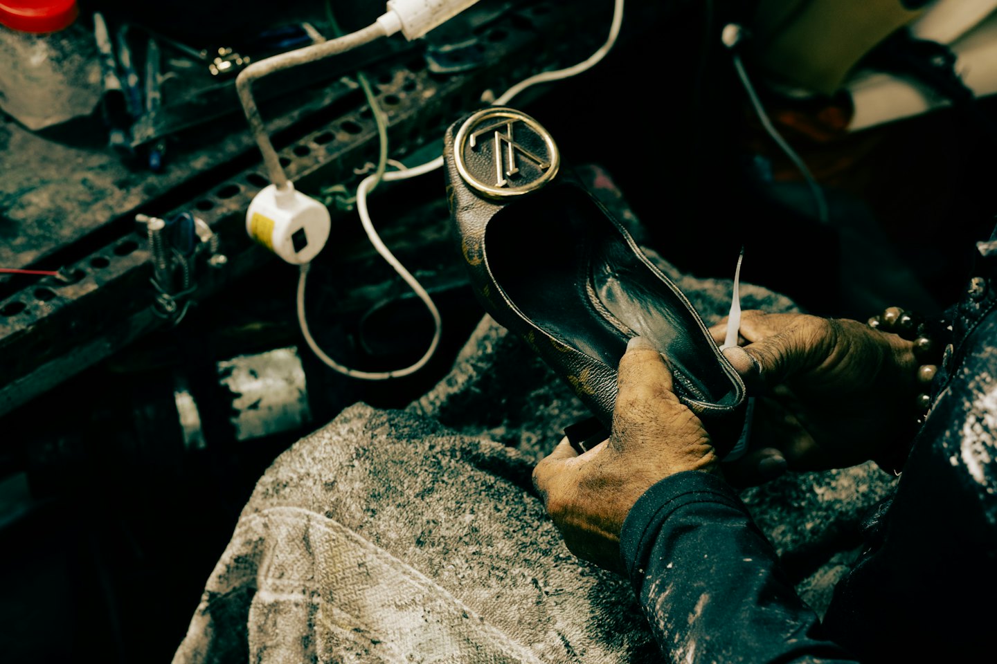 Hands repairing a brown leather designer shoe on a workbench.