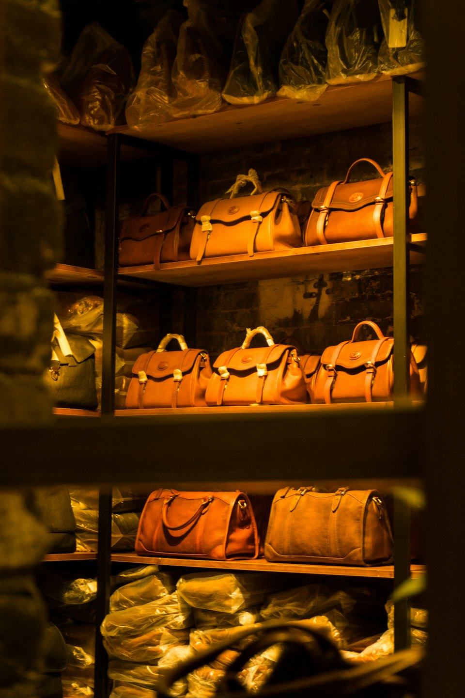 Brown leather handbags are organized neatly on wooden store shelves.