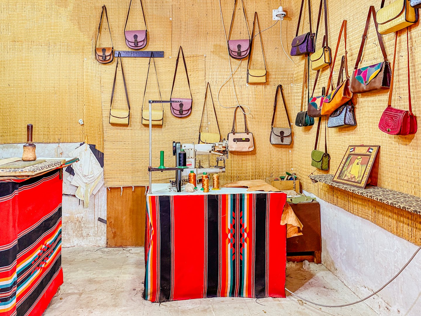 Handcrafted leather handbags hang above a workshop sewing station.