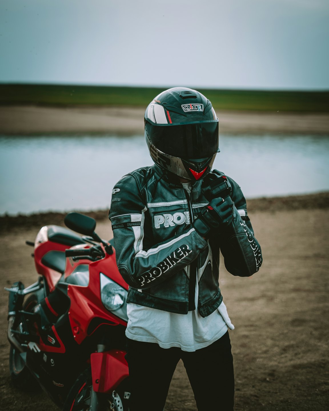 Motorcyclist adjusting gloves next to a red motorcycle outdoors.