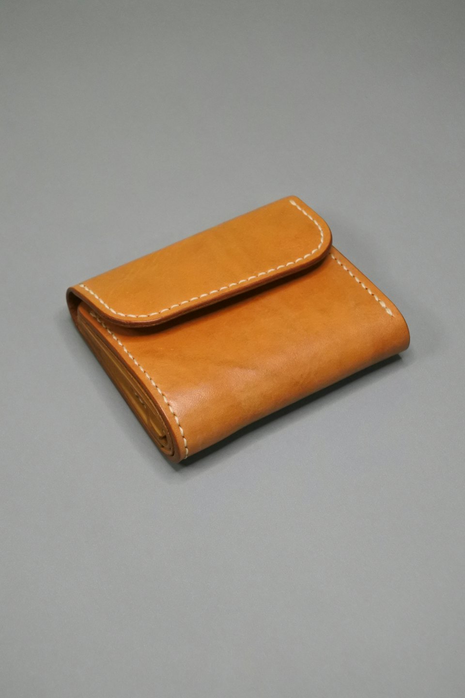 Closed light brown leather wallet with white stitching.
